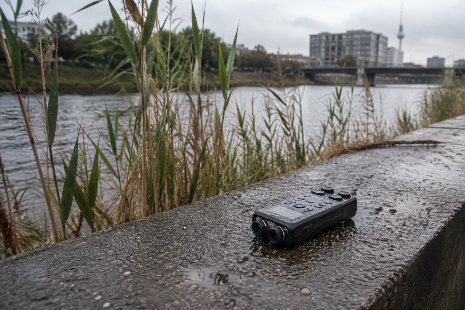 AI-generated editorial study of a field recorder beside water. Illustrative imagery, not documentation of an AER session.