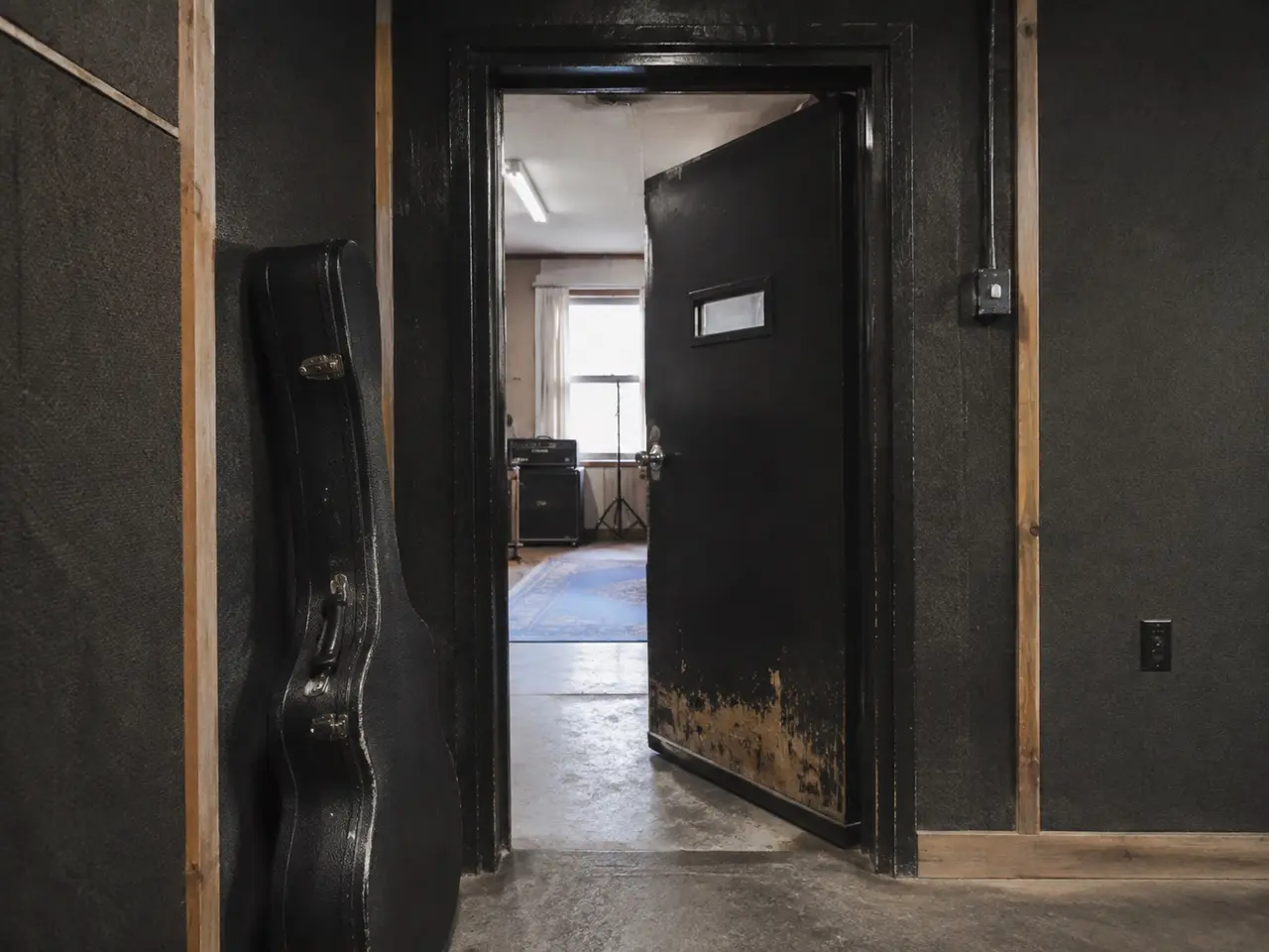 AI-generated study of a quiet rehearsal-room entrance and guitar case. Not an actual AER facility.